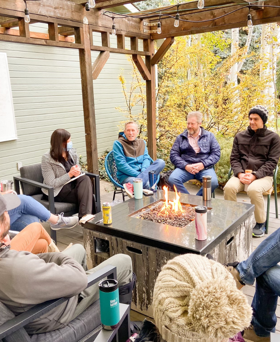Men and women sitting around a fire pit in autumn with coffee