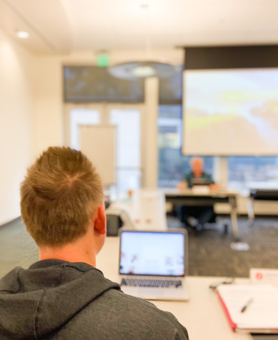 Photo taken from behind of a man sitting at a conference table with a laptop